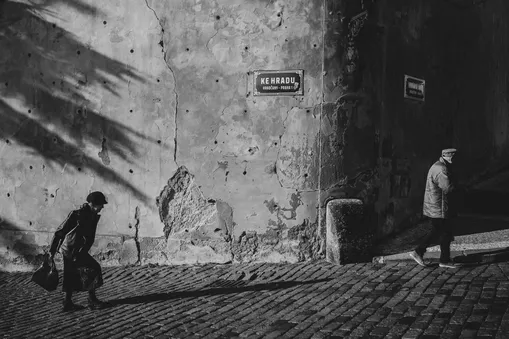 Černobílé street foto s lidmi procházejícími pražskou ulicí Ke Hradu na Hradčanech.