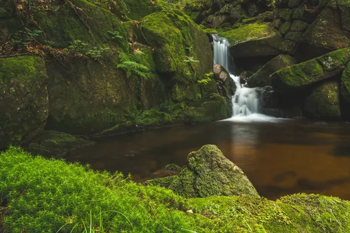 Lesní vodopád v Jizerských horách obklopený skalami porostlými sytě zeleným mechem.
