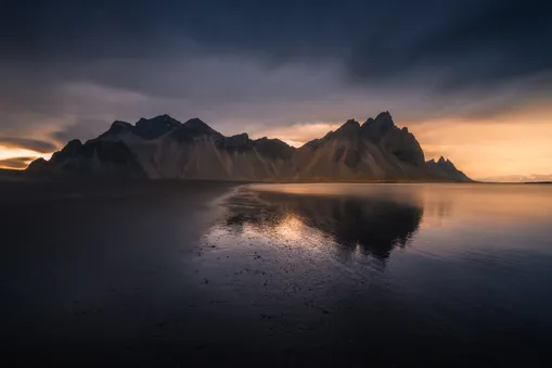Dramatické skalní štíty hory Vestrahorn na Islandu tyčící se nad temnou vodní hladinou po západu slunce.