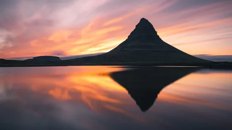 Dokonalý zrcadlový odraz hory Kirkjufell v klidné vodní hladině při oranžovém západu slunce na Islandu.