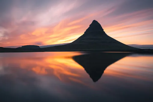 Dokonalý zrcadlový odraz hory Kirkjufell v klidné vodní hladině při oranžovém západu slunce na Islandu.