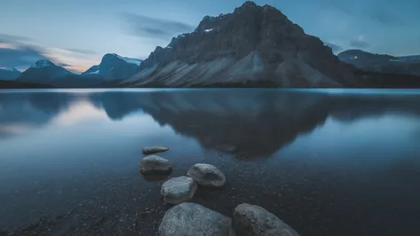 Zrcadlový odraz hory Crowfoot Mountain v klidné hladině jezera Bow Lake v Kanadě při ranním svítání.