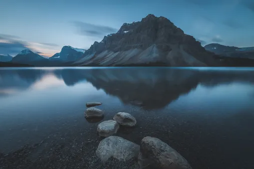 Zrcadlový odraz hory Crowfoot Mountain v klidné hladině jezera Bow Lake v Kanadě při ranním svítání.